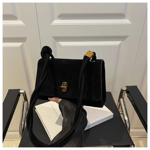 Detail of black suede crossbody bag with gold twist lock and thick rope strap on books