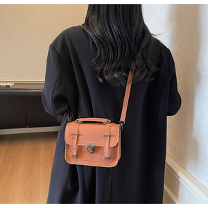 Orange textured small square crossbody bag shown on a model in a black suit