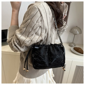 Détail d'un sac seau noir avec texture plissée brillante et accents de perles dorées