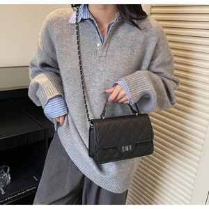 Detail of black quilted crossbody bag with silver twist lock and chain strap on model