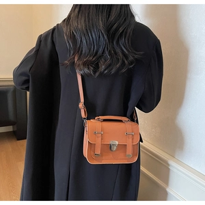 Detail of a brown leather crossbody tote bag with silver rotary lock and shoulder strap