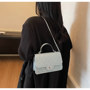 Detail of light blue quilted crossbody bag with silver metal chain on woman back