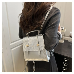 Silver metallic backpack with woven texture details shown on a model in a home setting