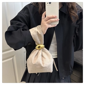 Detail of beige suede handbag featuring a large sculptural gold buckle and knot closure