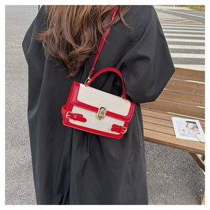 Detail of red and cream contrast crossbody bag with gold metal clasp on a black coat