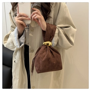 Detailed view of brown suede bucket bag featuring a unique golden metal handle and soft pleats