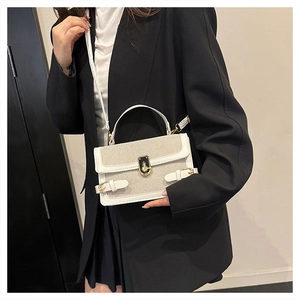 Detail of a minimalist square bag featuring white leather, beige fabric, and gold hardware