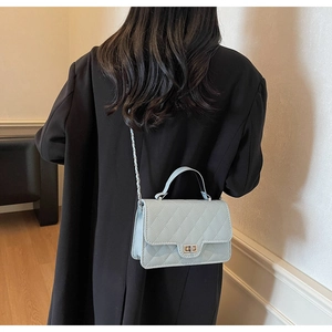 Detail of light blue quilted crossbody bag with silver chain strap on a black coat
