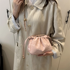 Sac seau rose à cordon avec bandoulière dorée porté sur un manteau beige