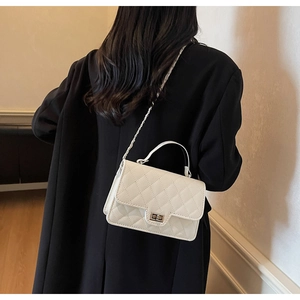 Detailed view of a white quilted square crossbody bag with metallic twist lock and chain strap