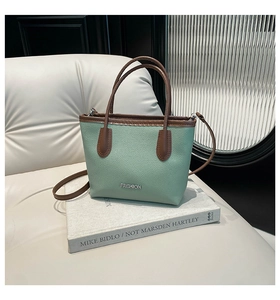 Detail of mint green pebbled leather bucket bag with brown handle and FASHION logo