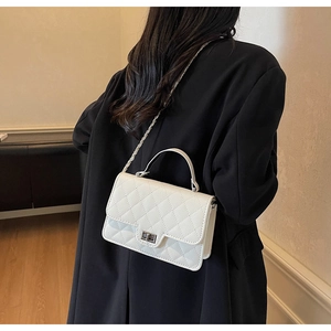 Close-up of a white quilted chain bag worn over the shoulder on a black coat back view
