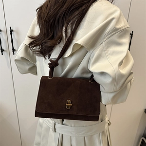 Brown suede crossbody bag with gold knob closure and knotted strap on beige trench coat