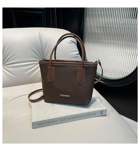 Detail of dark brown lychee textured handbag with fashion silver logo and shoulder strap