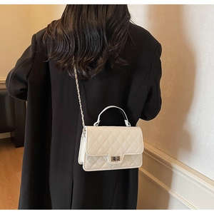 Detail of a beige quilted square bag with gold twist lock and chain strap on a black coat