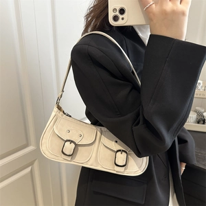 Minimalist beige baguette bag with front pockets and black metal buckles shown in mirror selfie