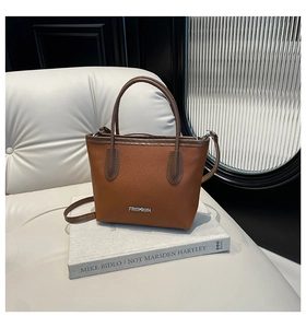 Close-up of brown lychee grain leather handbag with silver Fashion lettering on white sofa