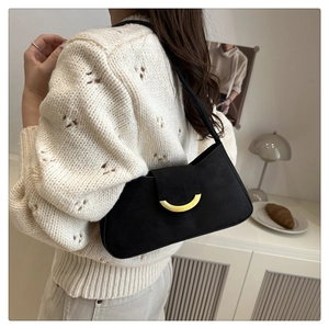 Close-up of black suede underarm bag with gold semicircular buckle on a white sweater