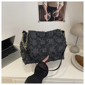 Detail of black textured tassel crossbody bag with gold chain and quilted square pattern