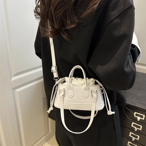 Minimalist white crocodile embossed bucket bag shown as a crossbody on a model