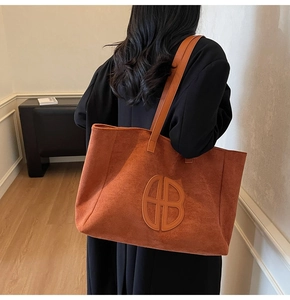 Detail of large orange suede tote bag featuring unique circular embossed leather patch logo