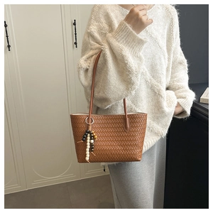 Close-up of brown woven leather tote bag with stylish wooden bead pendant detail