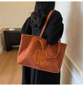 Close-up of the orange suede tote bag featuring a circular logo and slim shoulder strap