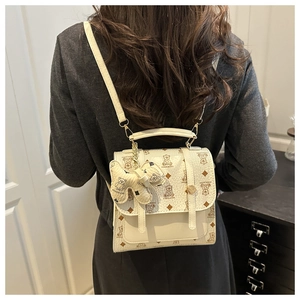 Rear view of model wearing a beige mini backpack with bear patterns and charm