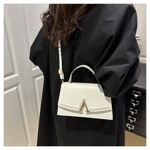 Detail of white minimalist crossbody bag with gold V-buckle on black outfit context