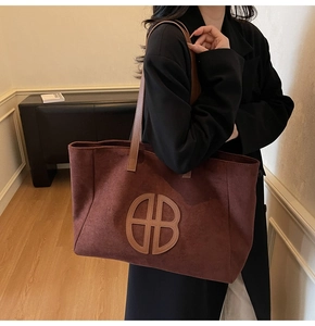 Detail of burgundy suede tote bag with circular cutout logo and brown leather handle