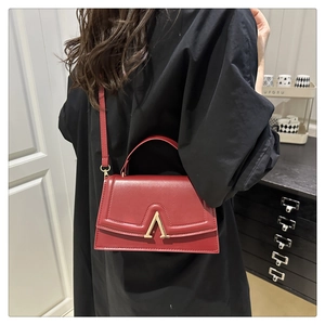 Detail of red leather square handbag with a gold A-letter lock on model's shoulder