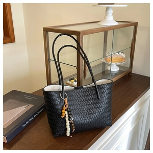 Close-up of black woven leather tote bag with unique wood bead tassel charm detail