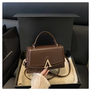 Detail of dark brown leather handbag with gold A-clasp in premium gift box packaging