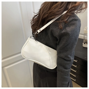 White glossy patent leather baguette shoulder bag shown on model in a modern interior
