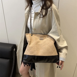 Quilted beige and black tote bag with metal chain strap worn on beige trench coat