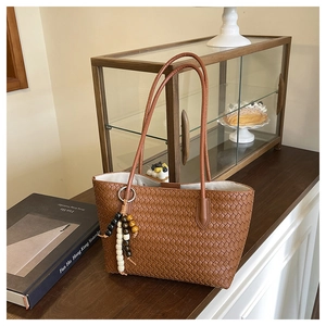 Detail of a brown woven shoulder bag with beaded tassel on a vintage wooden desk