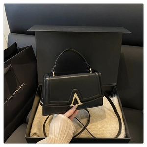 Close-up of black crossbody bag with gold V-shaped buckle and luxury gift packaging