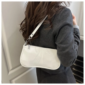 Close-up of a white patent leather baguette bag with silver hardware on a model's shoulder