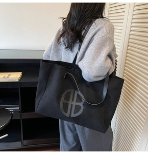 Detail view of large black matte tote bag with embossed logo worn on the shoulder