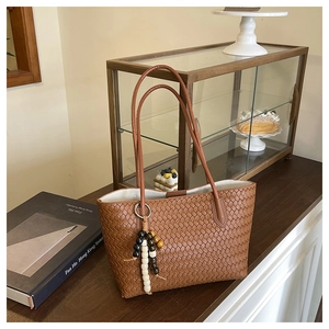 Detail of a brown woven leather tote bag featuring a colorful beaded tassel charm