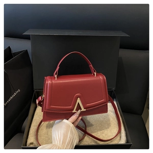 Detail of red square handbag with V-shaped gold buckle and premium gift packaging