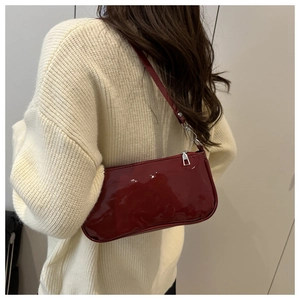 Detail of dark red glossy patent leather shoulder bag worn over a beige knit sweater