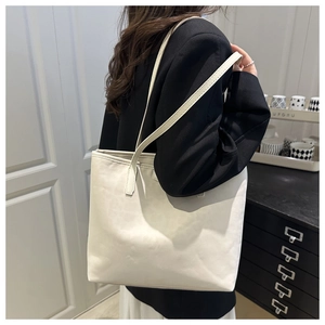 Detail view of large cream tote bag with slim shoulder straps on black blazer