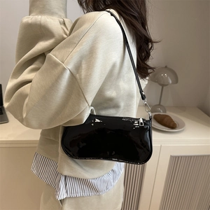 Chic black patent leather shoulder bag for women shown on model in a cozy indoor setting