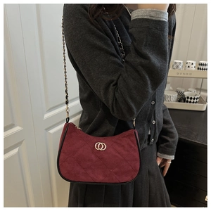 Detail of burgundy quilted suede shoulder bag with gold double-ring hardware on a model
