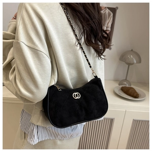 Close-up of black quilted suede chain bag worn by a model in warm lighting