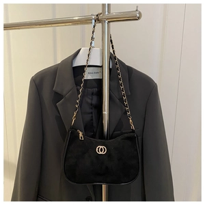 Detail of black quilted suede shoulder bag with golden hardware on a grey suit jacket