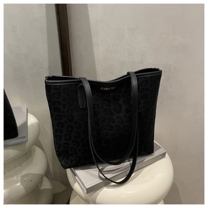 Detail of a dark leopard print tote bag with gold label on a minimalist white stand