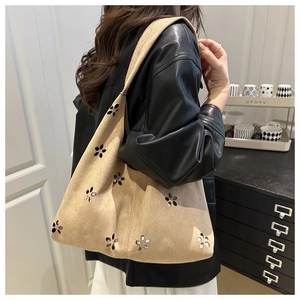 Detail of laser-cut floral patterns on a large suede beige tote bag worn by a model
