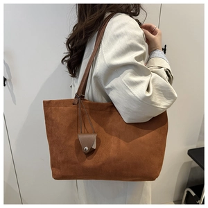 Detail of brown large capacity tote bag featuring soft suede texture and leather charm detail
